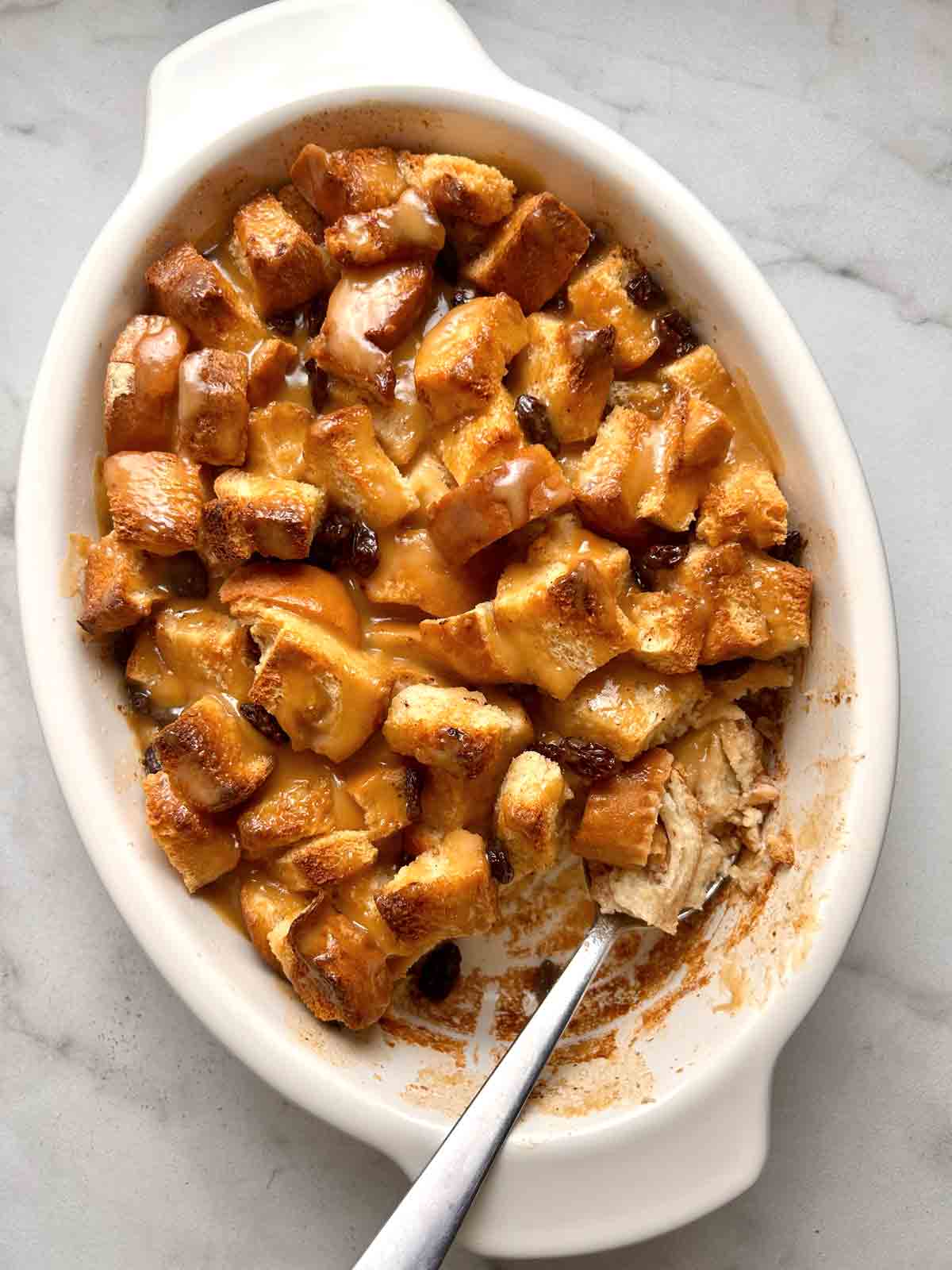 finished bread pudding with portion scooped out of it in baking dish.