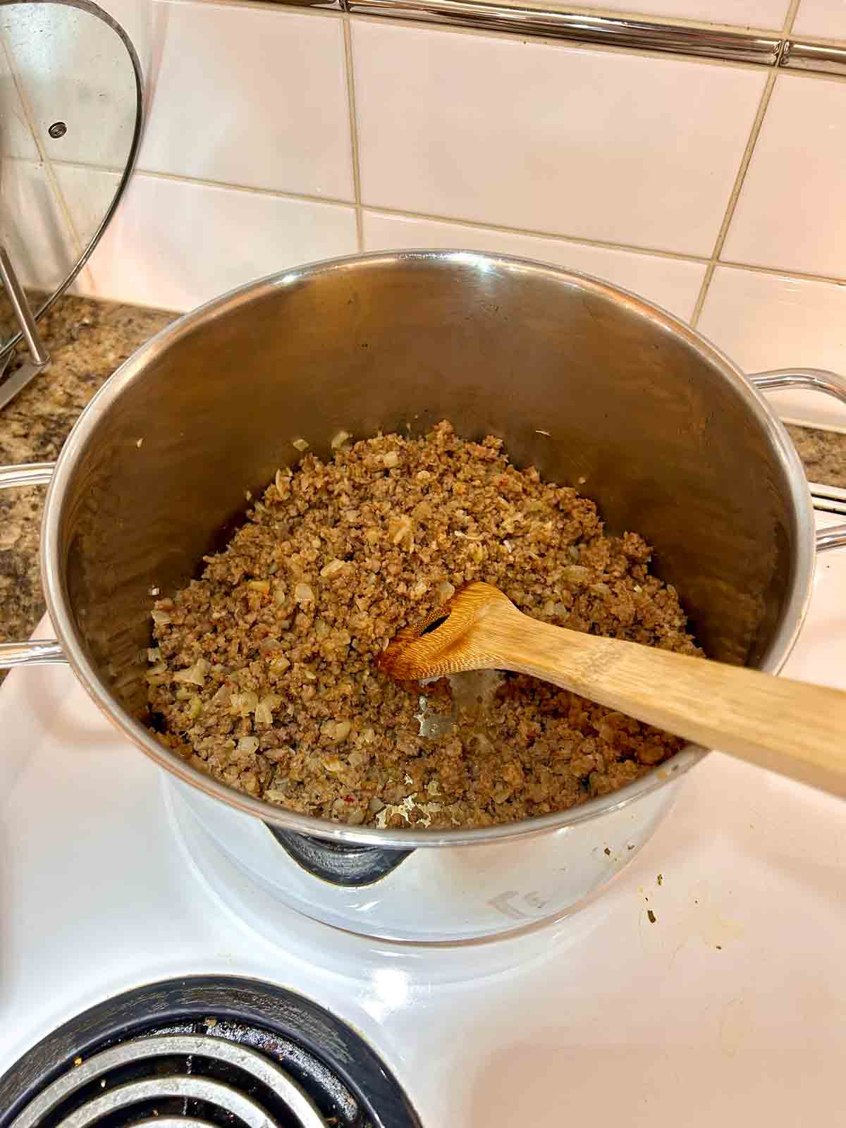 Italian sausages, onion, and garlic being cooked in pot.