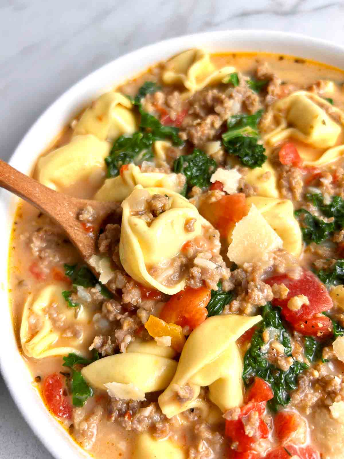 spoon lifting sausage tortellini soup from bowl.