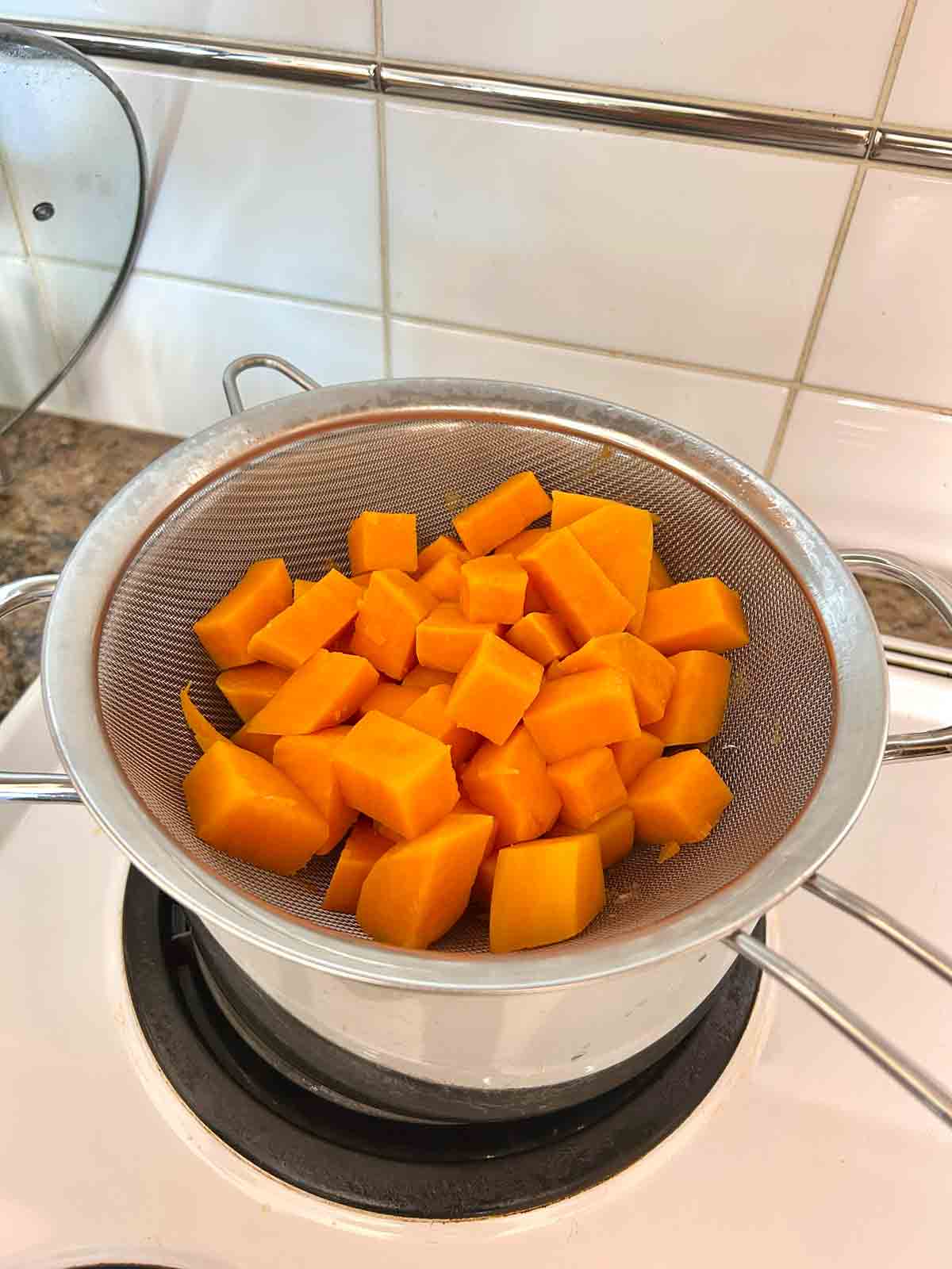 cubed sweet potatoes boiled and draining over pot.