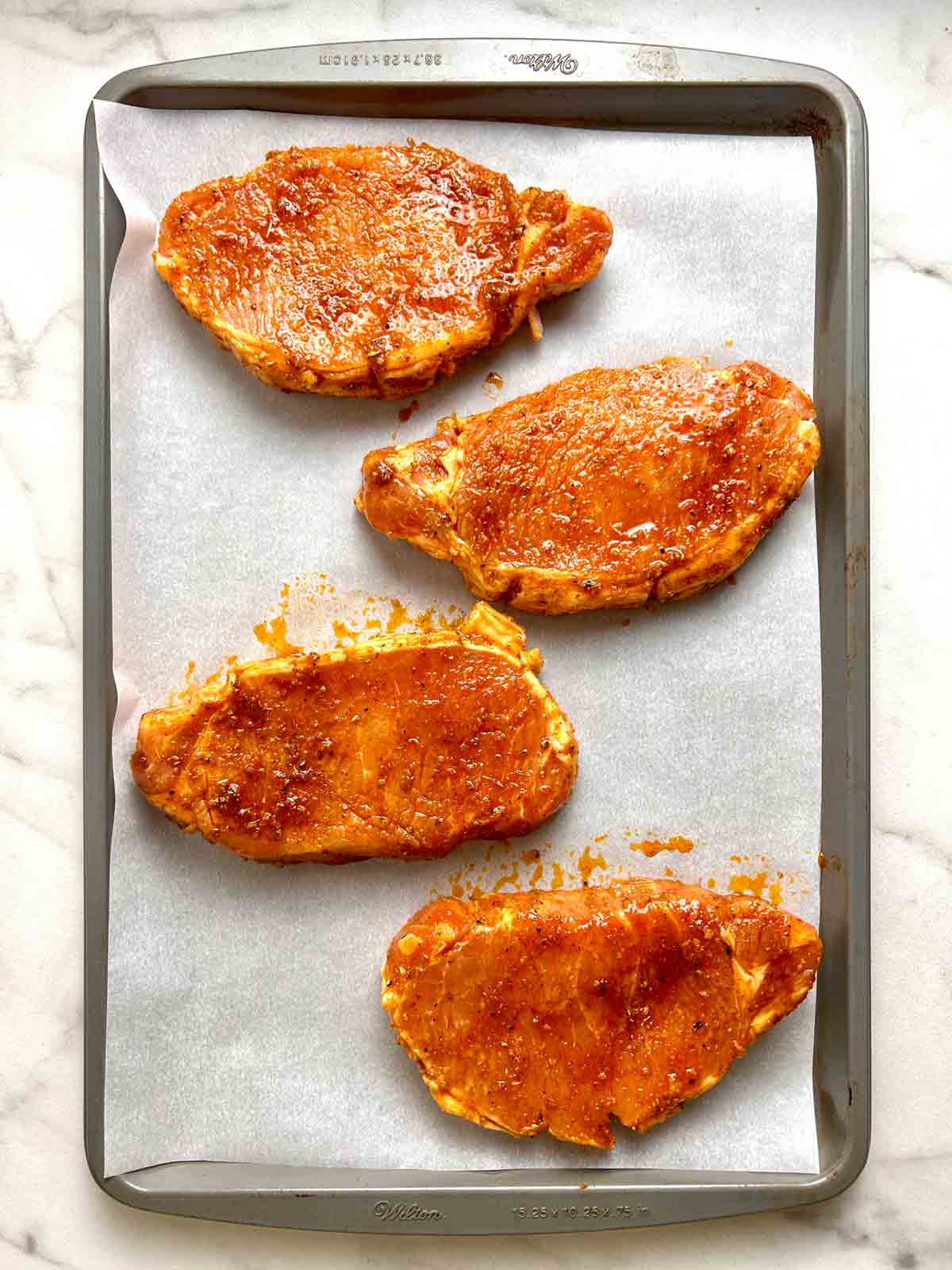 marinated pork chops arranged on baking sheet.