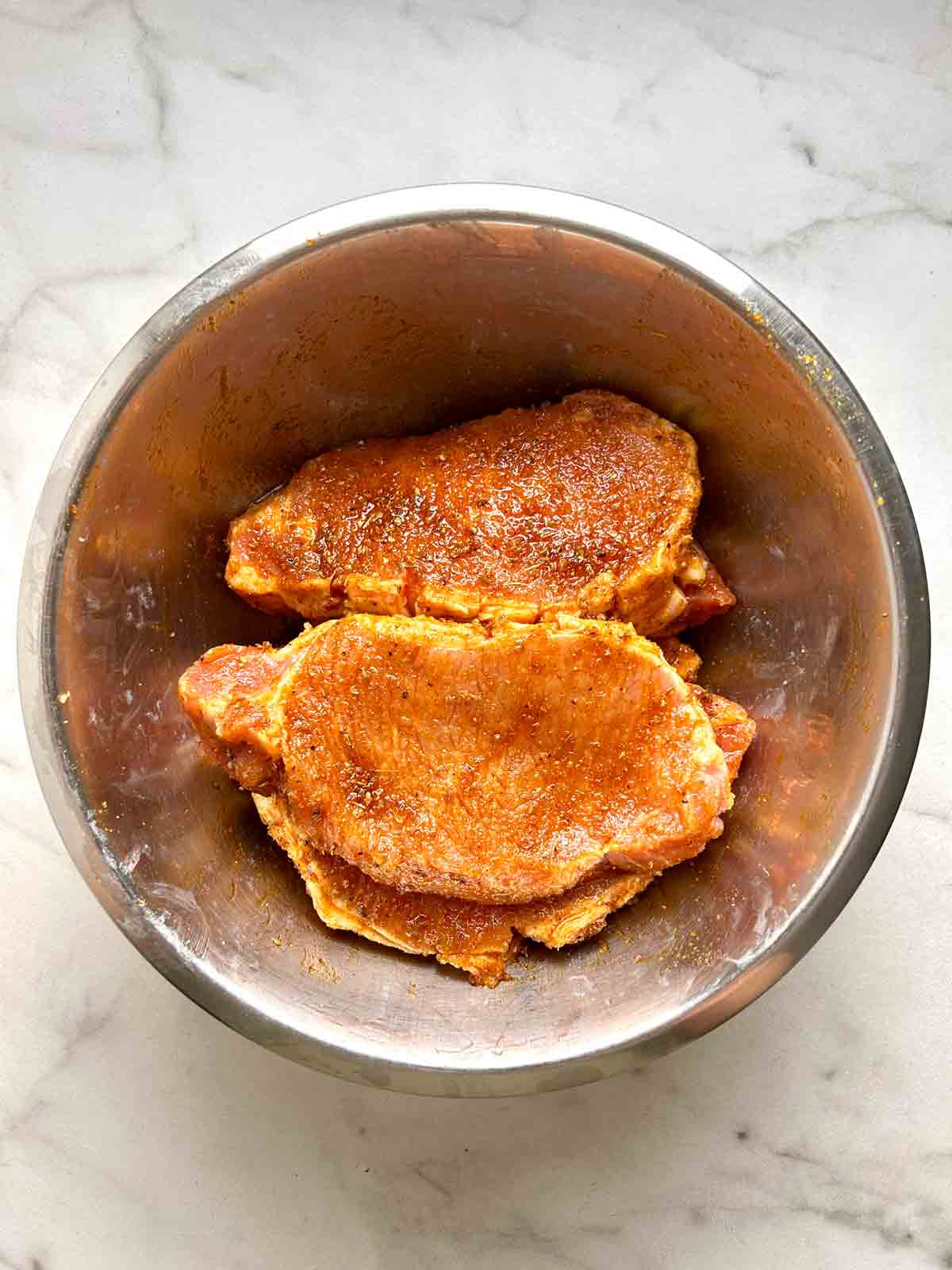 pork chops rubbed with marinade in bowl.
