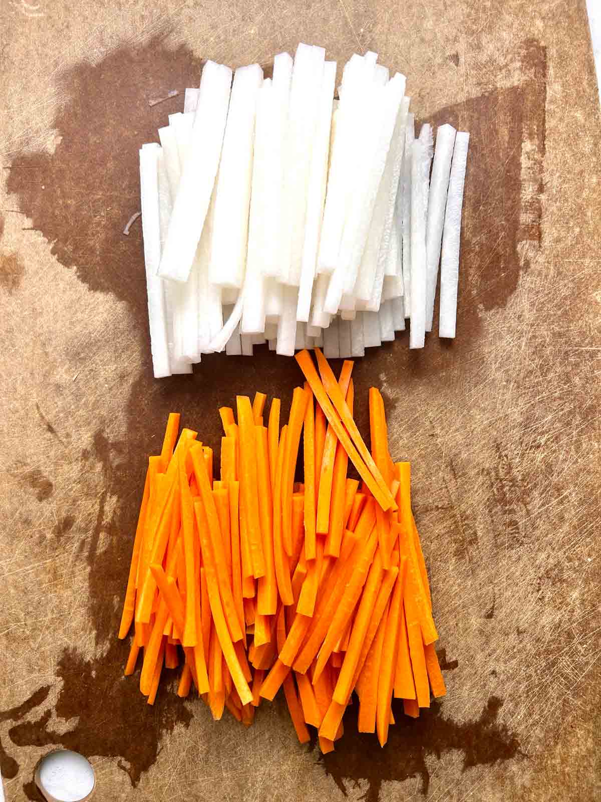 daikon and carrots cut into matchsticks on cutting board.