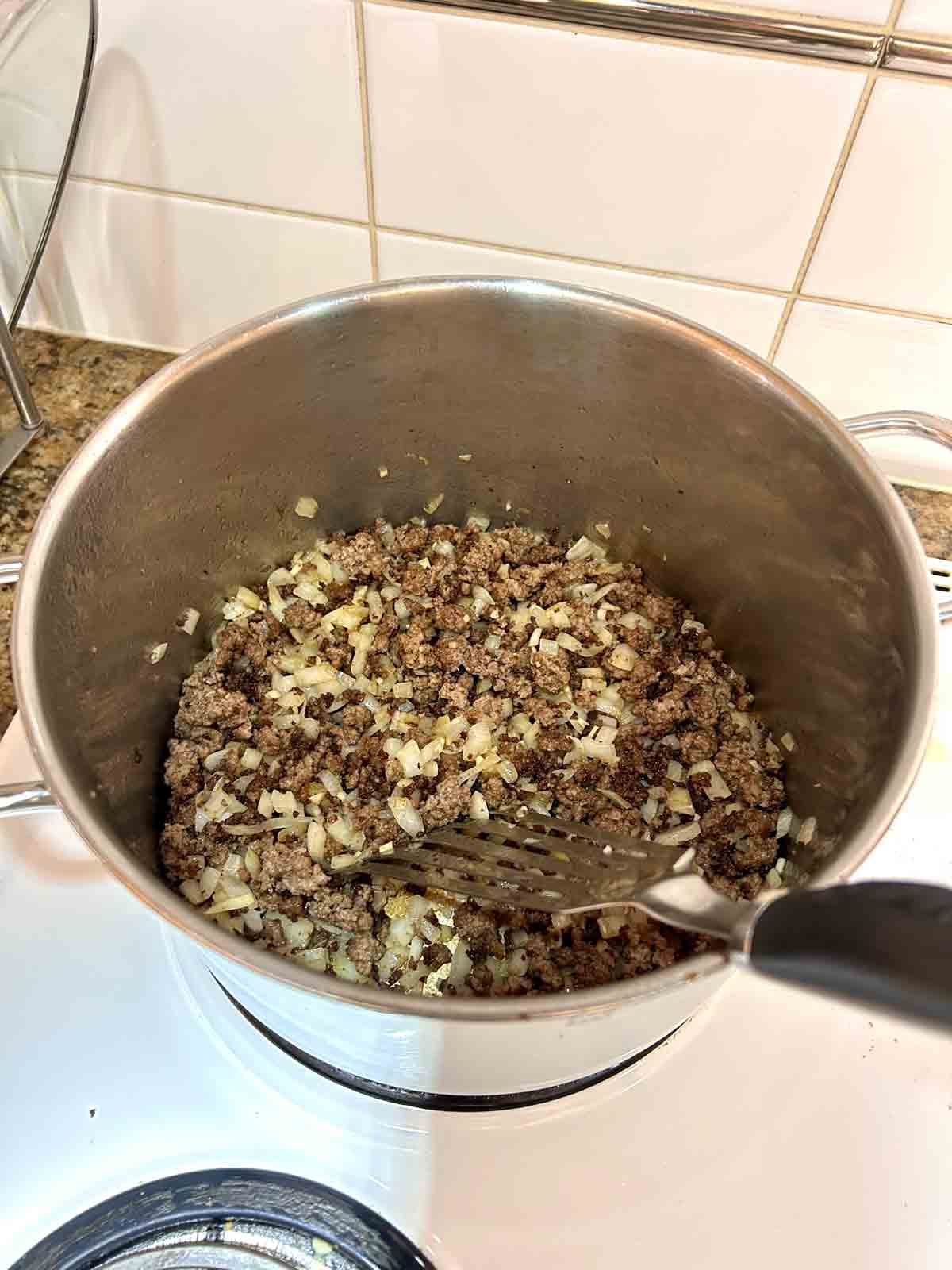 beef, onions, and garlic sautรฉing in pot.