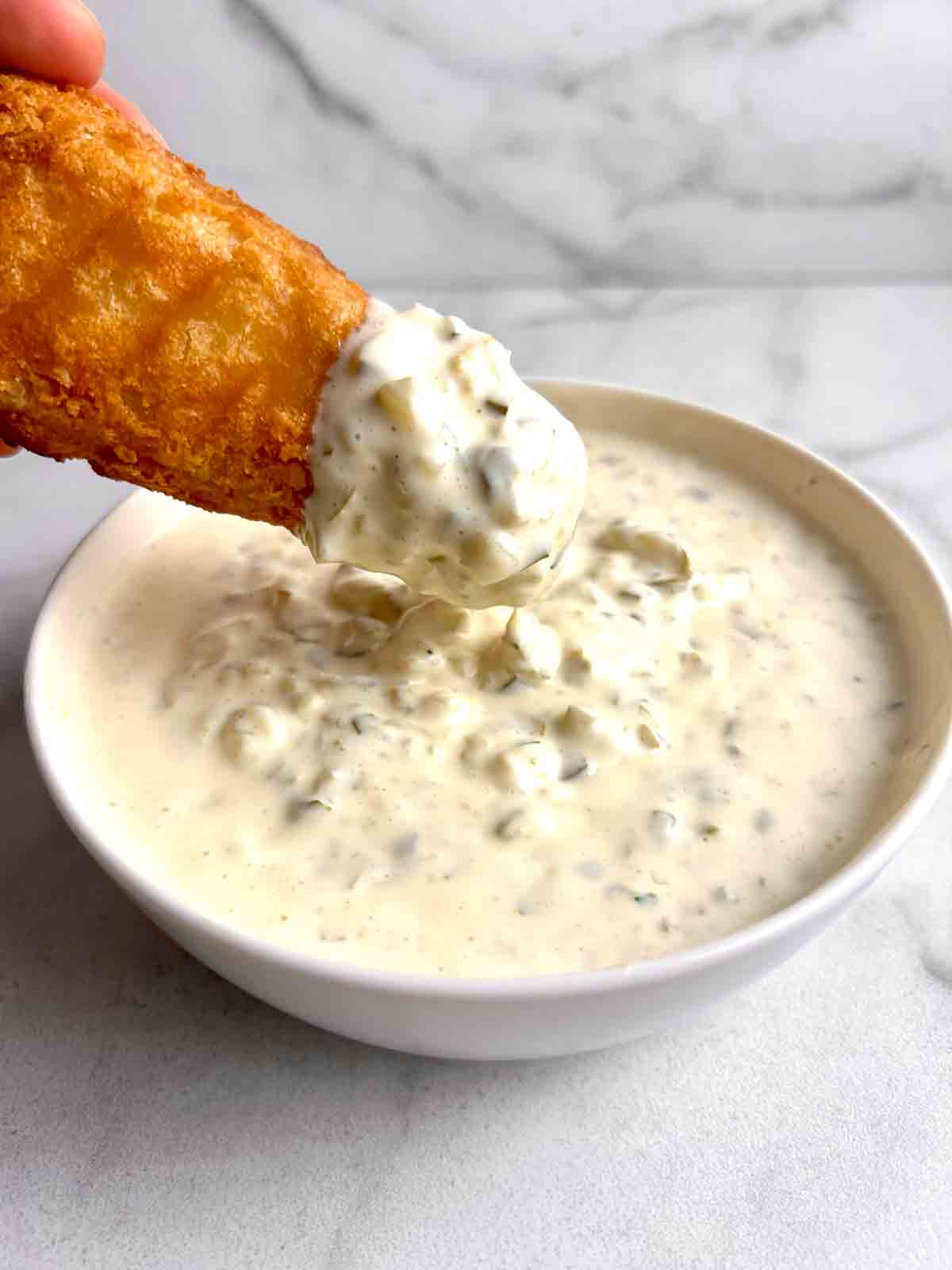 fried fish being dipped into bowl of tartar sauce.