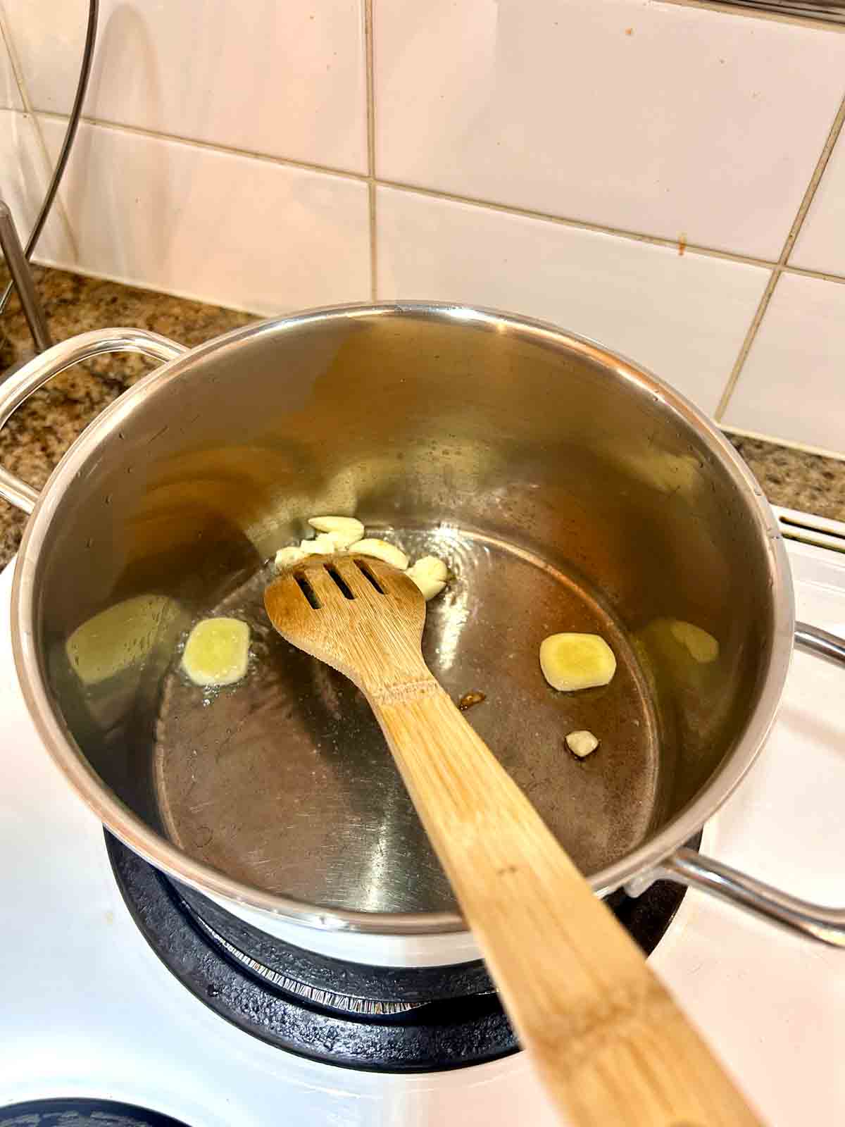 garlic and ginger being sautรฉed in oil in medium pot.