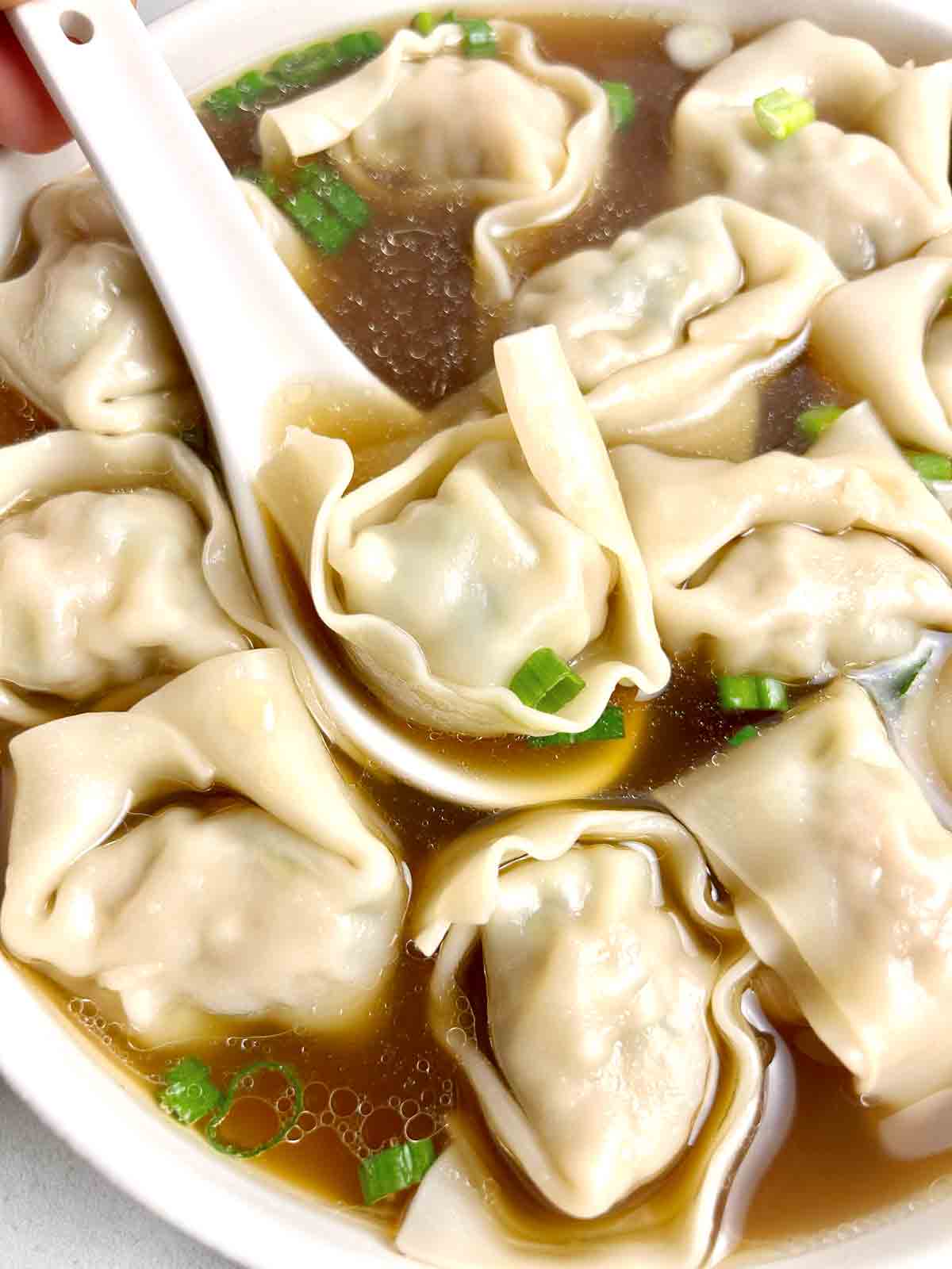 spoon lifting wonton from bowl of wonton soup.