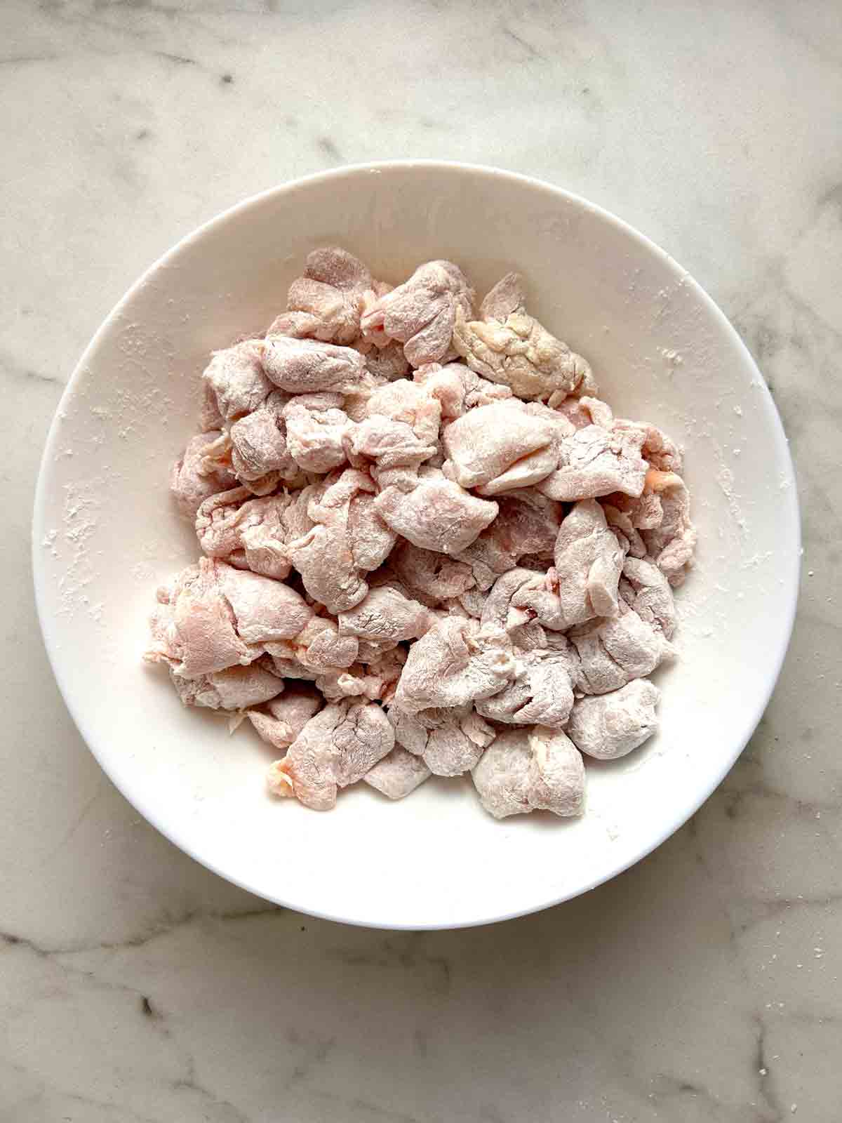 chicken pieces coated with cornstarch in bowl.