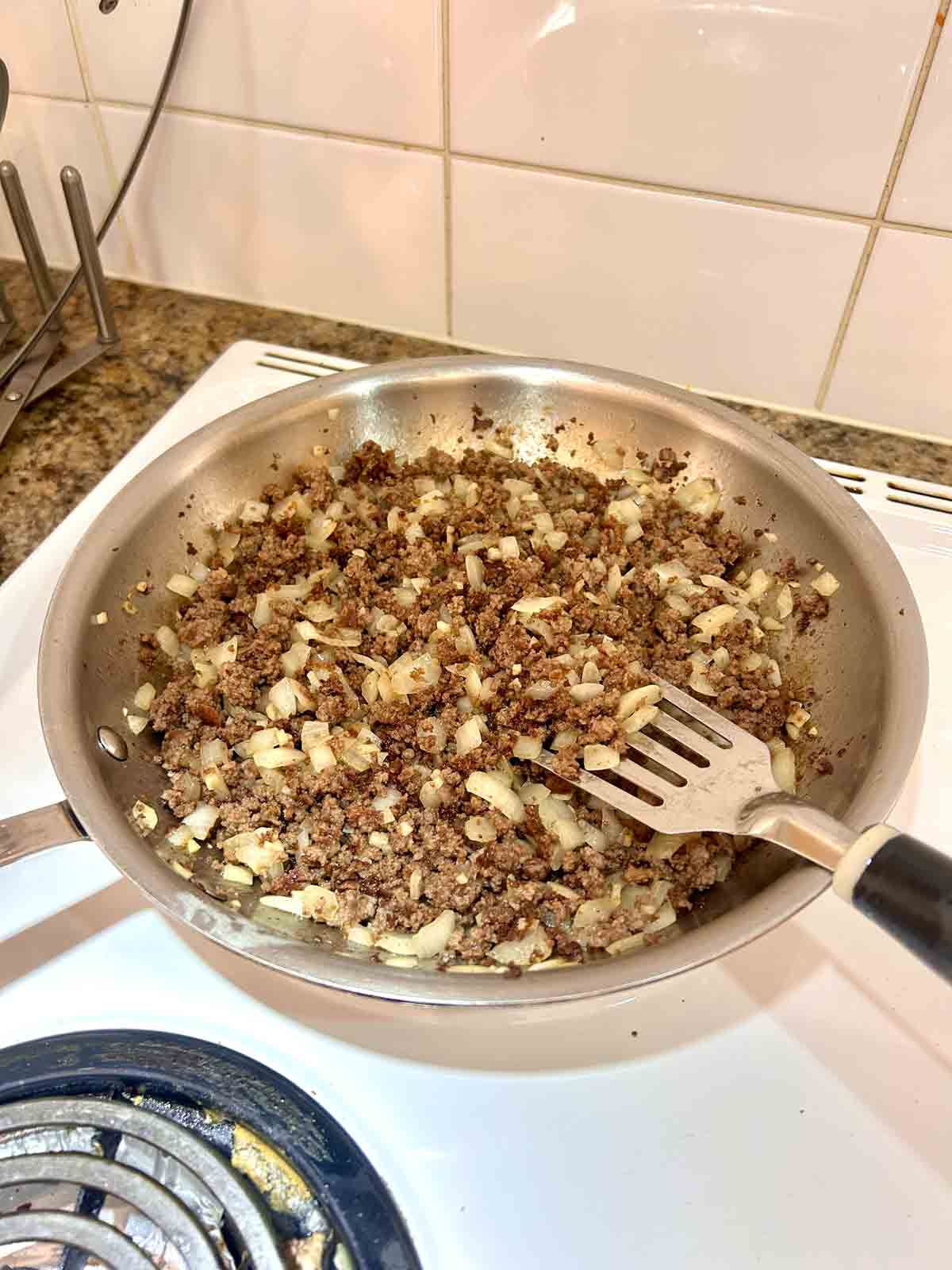 beef, onions, and garlic cooking in pan.
