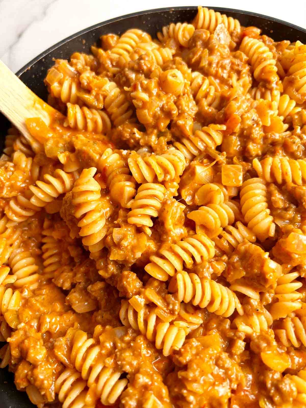 lifting taco pasta from skillet with wooden spoon.