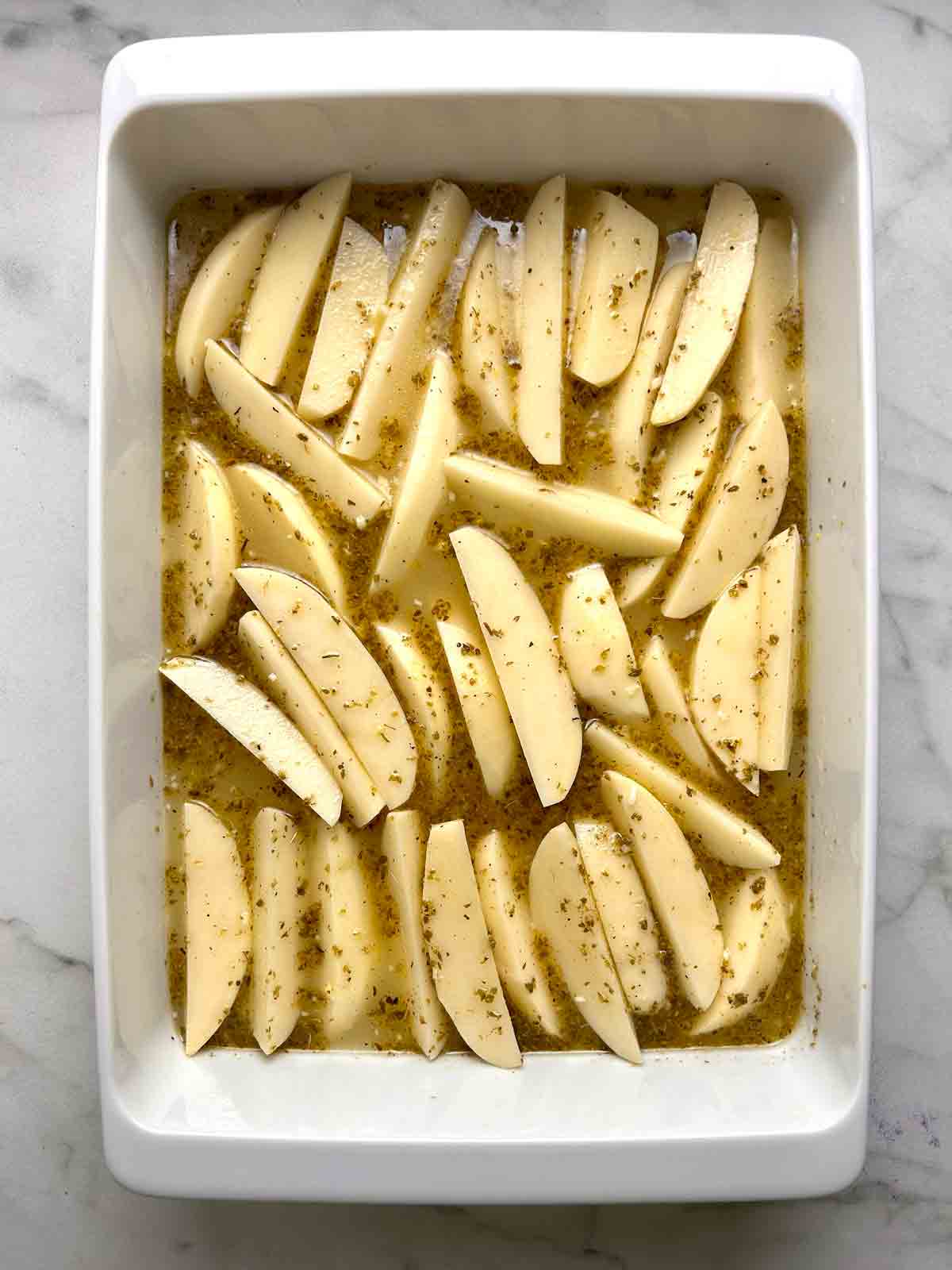 potato wedges mixed with lemon garlic broth in baking dish.