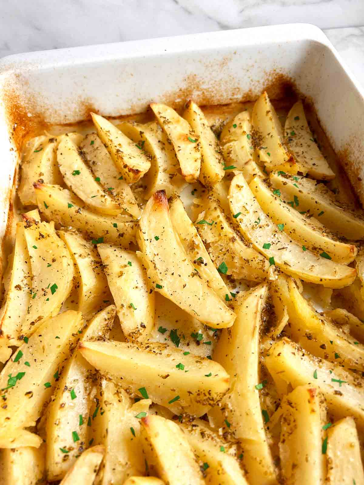 close up of Greek potatoes in baking dish with chopped parsley garnished on top.