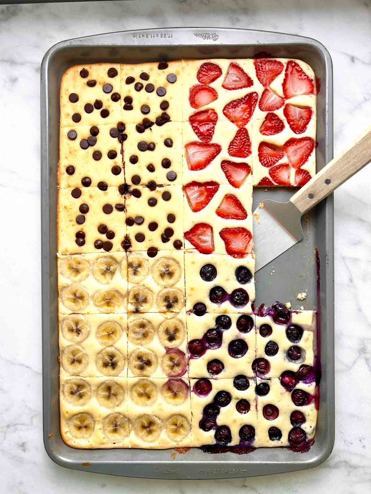 sheet pan pancakes cut into slices with spatula on pan.