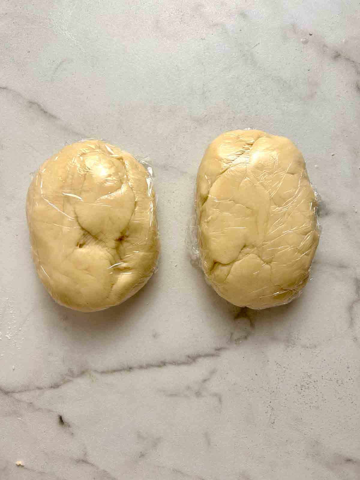 dough divided into two pieces and wrapped with plastic.