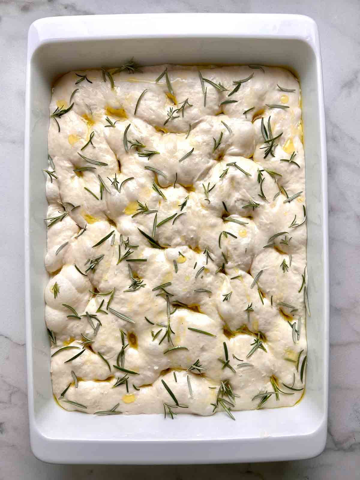 dimples pressed into dough and rosemary and salt sprinkled on top.