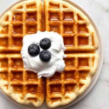 sourdough waffles on plate with dollop of cream and blueberries.