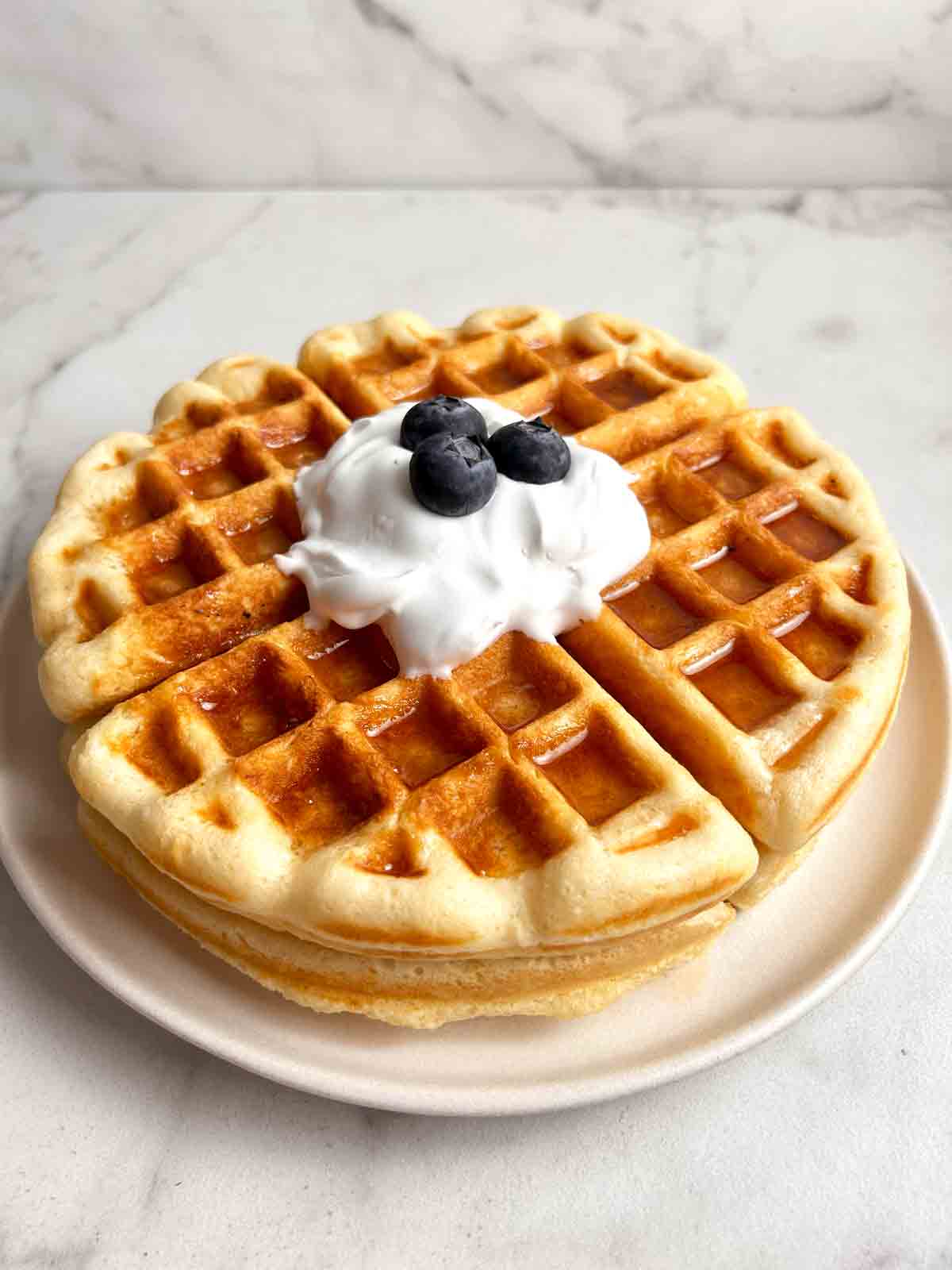 sourdough waffles on plate with dollop of cream and blueberries.