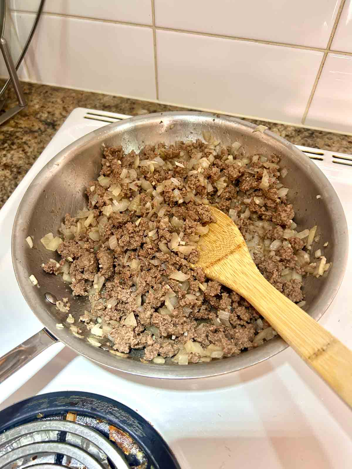 ground beef, onions, and garlic being cooked in skillet.