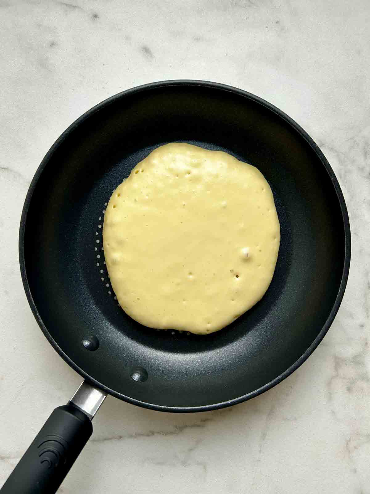 first side of pancake being cooked in pan.