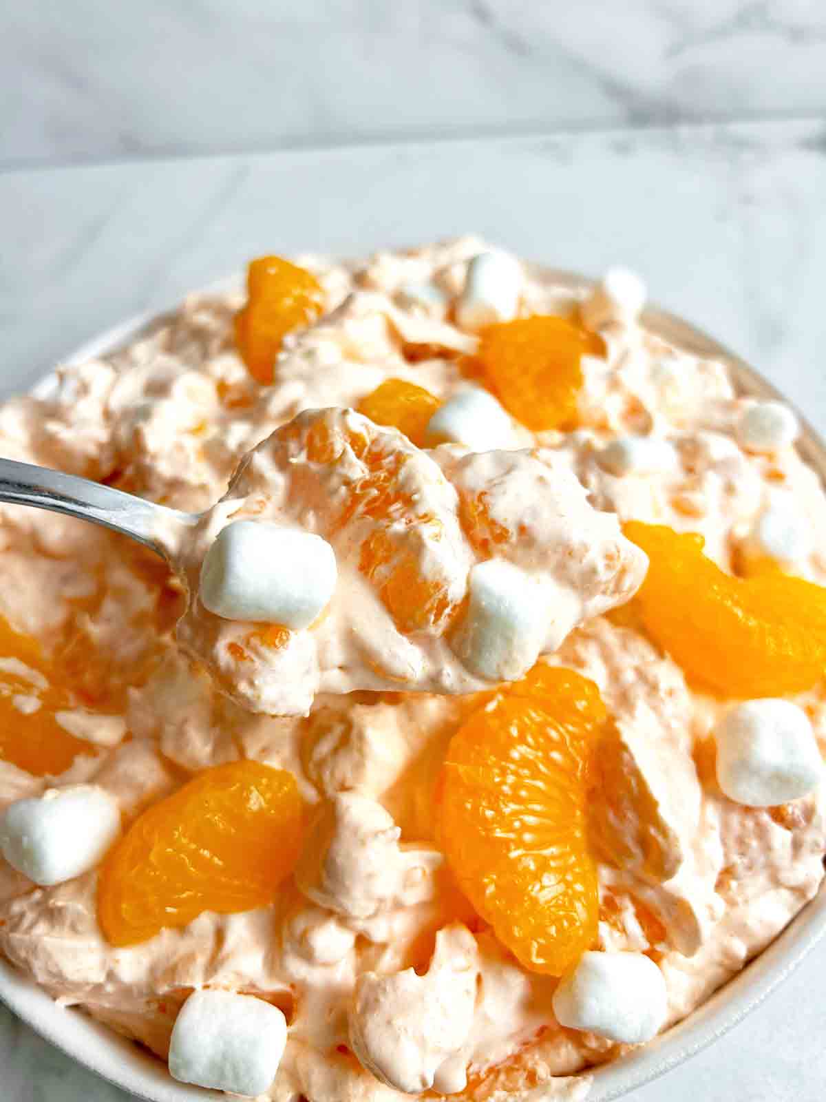 spoon lifting orange fluff salad from bowl.