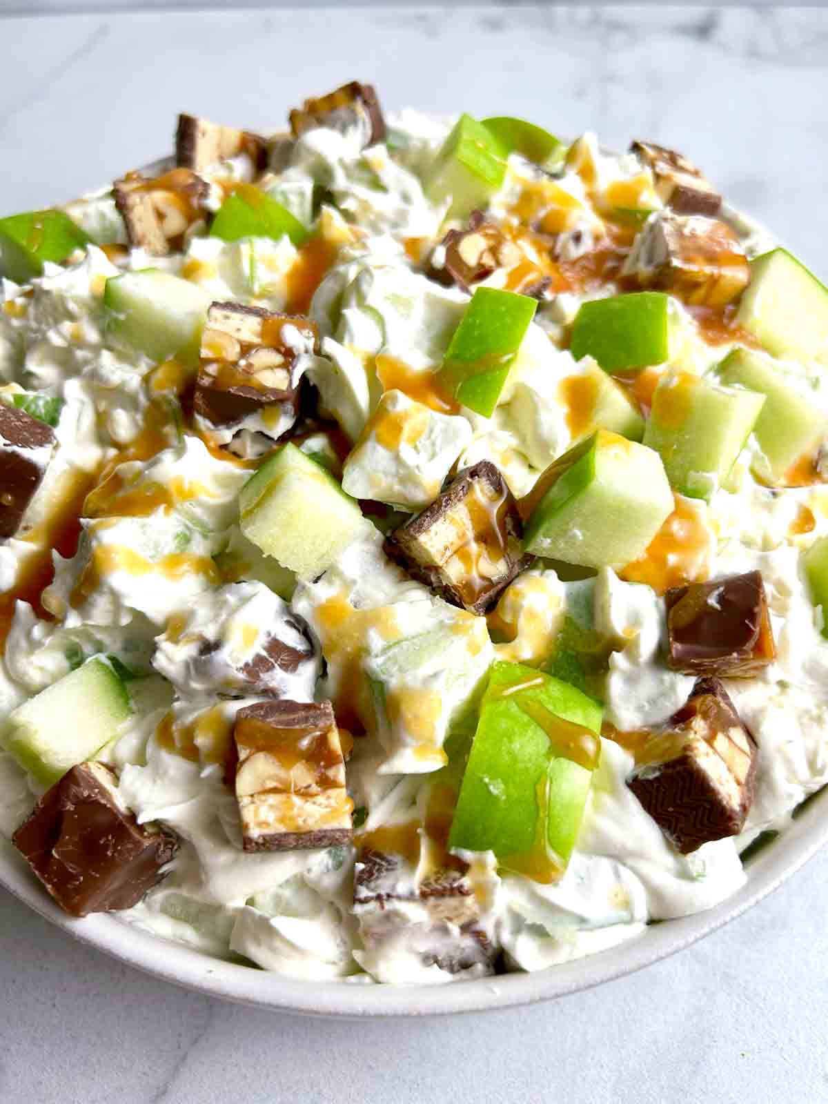 close up bowl of Snickers salad with caramel drizzled on top.