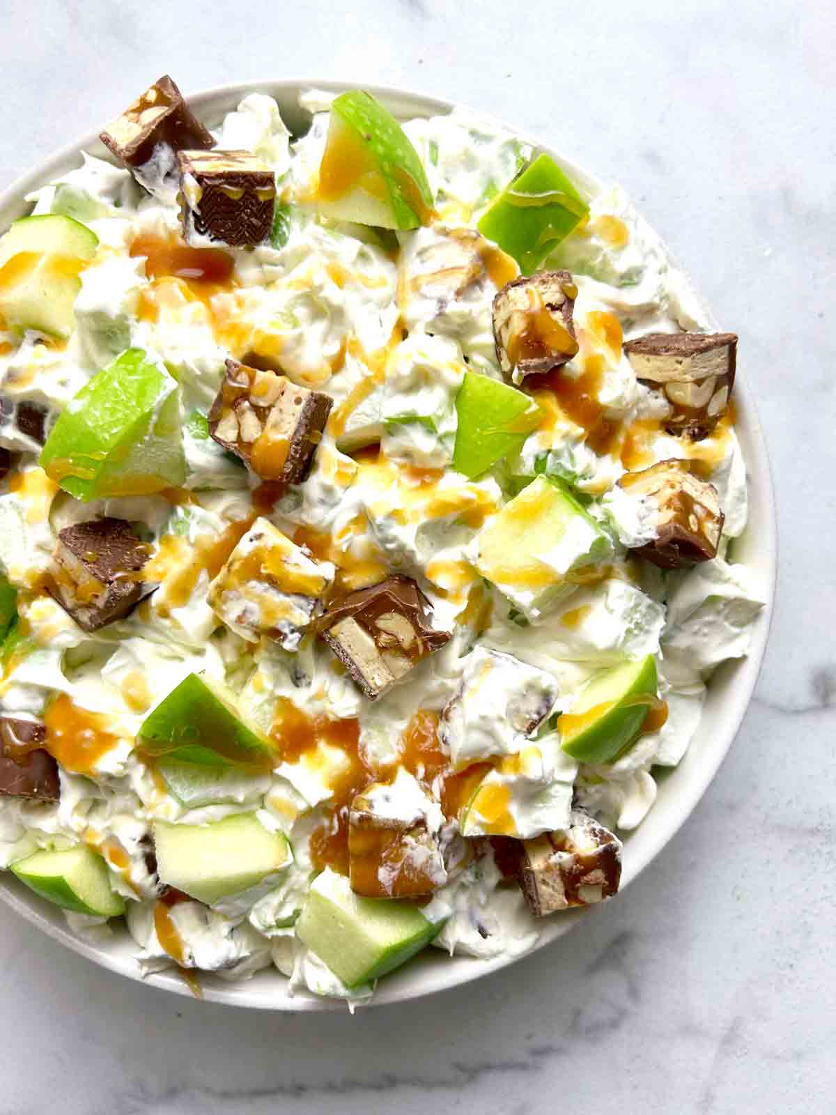 bowl of Snickers salad with caramel drizzled on top.