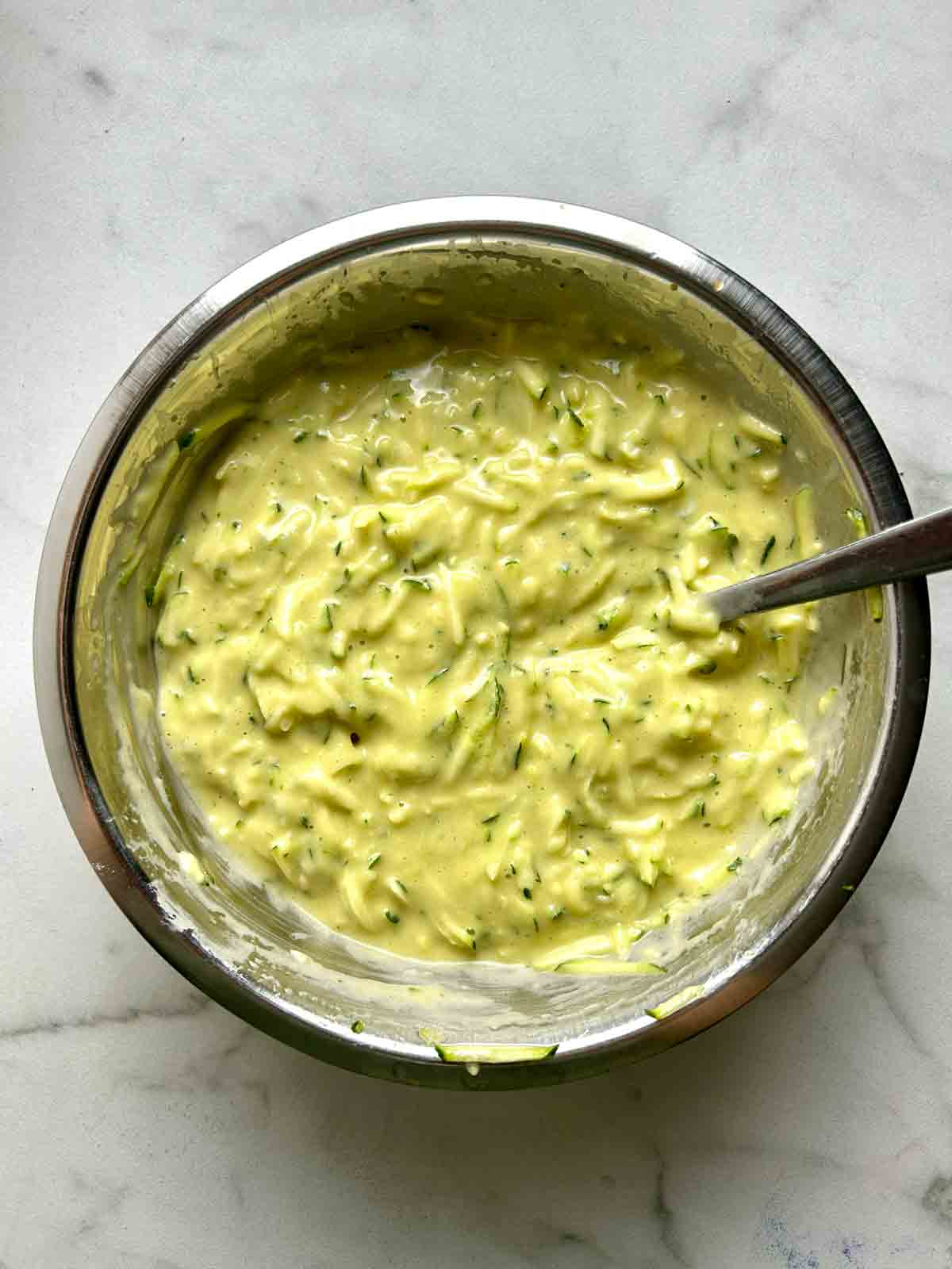 zucchini whisked with other wet ingredients in bowl.