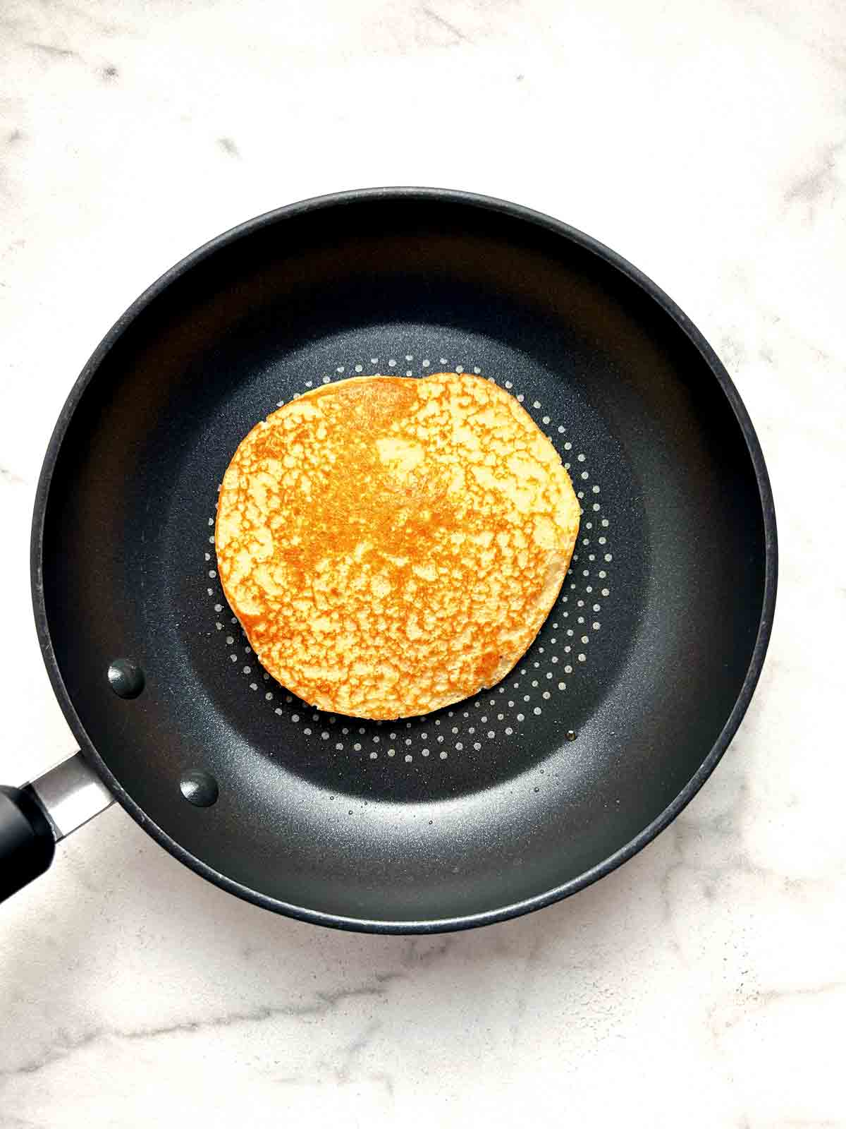 pancake flipped over in pan to show the golden brown inside.