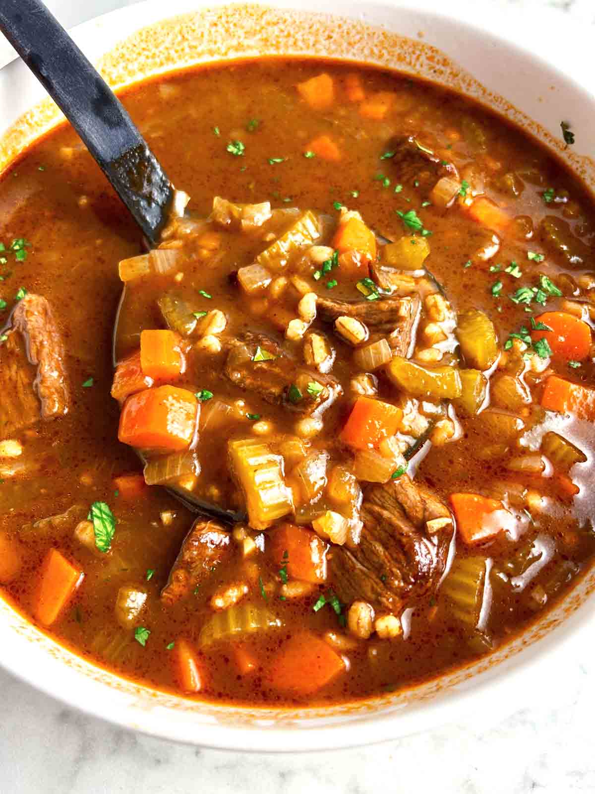 ladling beef barley soup from big bowl.