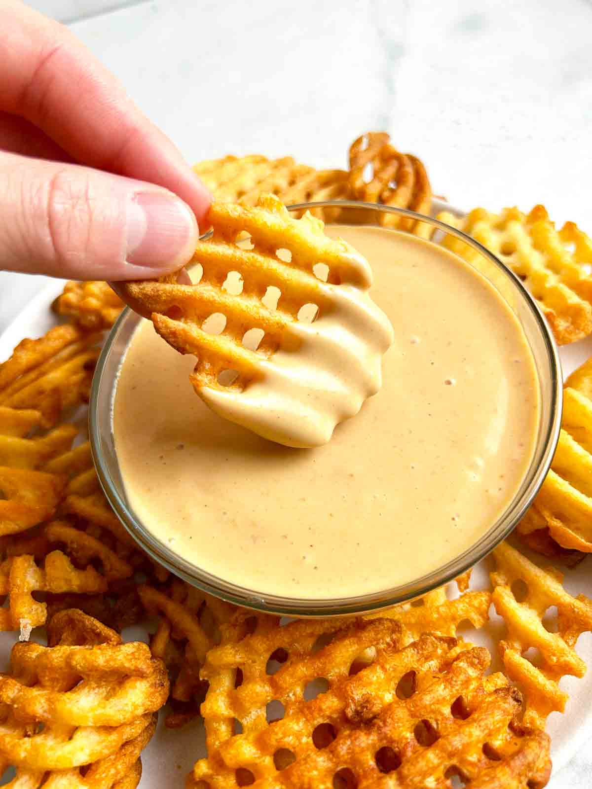 waffle fry being dipped into bowl of chick-fil-a sauce.
