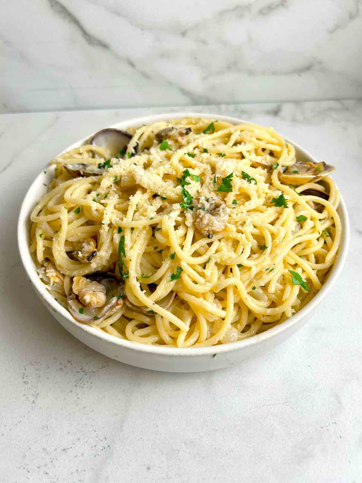 bowl of clam pasta with parsley and parmesan cheese sprinkled on top.