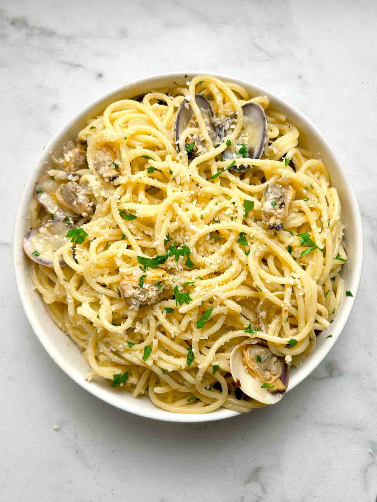 overhead shot of clam pasta with parsley and parmesan cheese sprinkled on top.