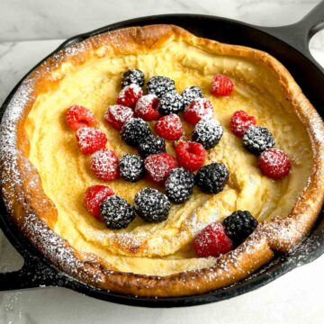 Dutch baby still in pan with berries and powdered sugar on it.