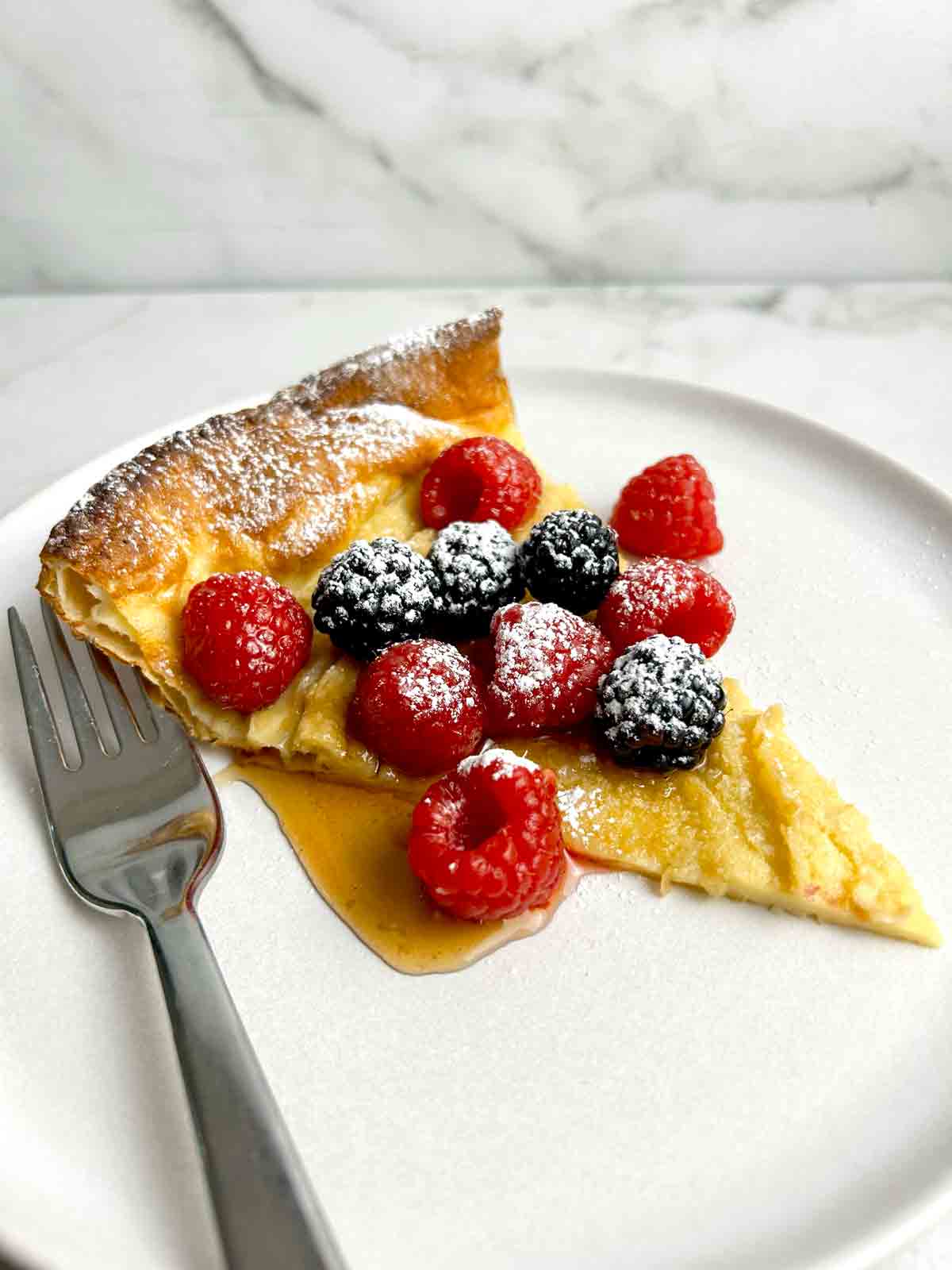 slice of Dutch baby with berries, syrup, and powdered sugar.