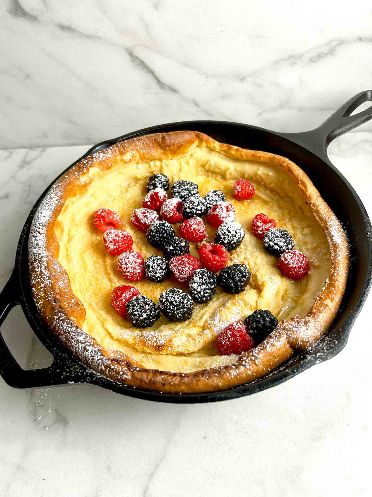 Dutch baby still in pan with berries and powdered sugar on it.