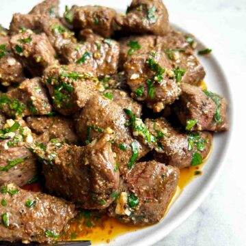close up of air fryer steak bites with garlic butter on plate.