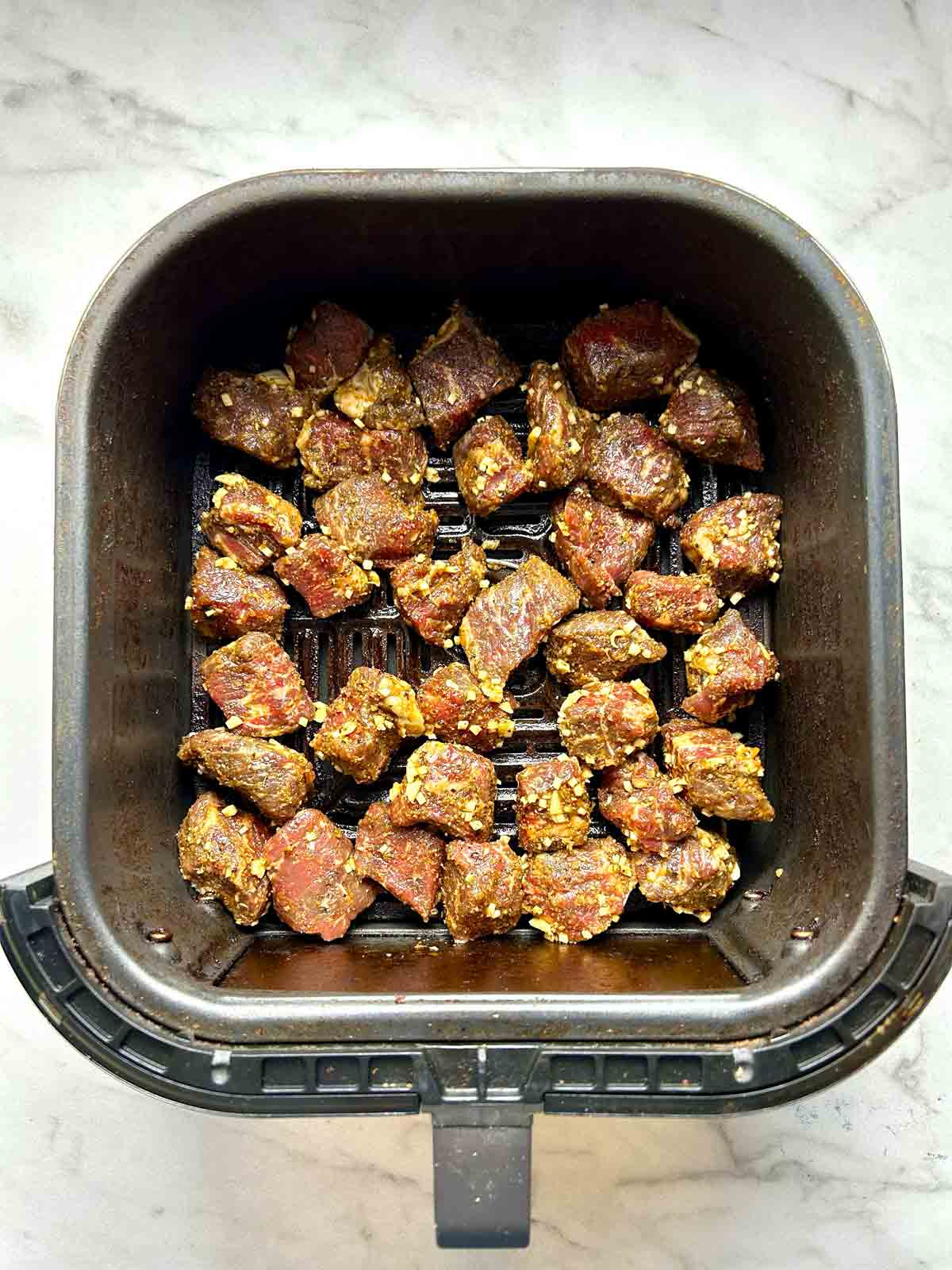 seasoned steak spread in air fryer basket.