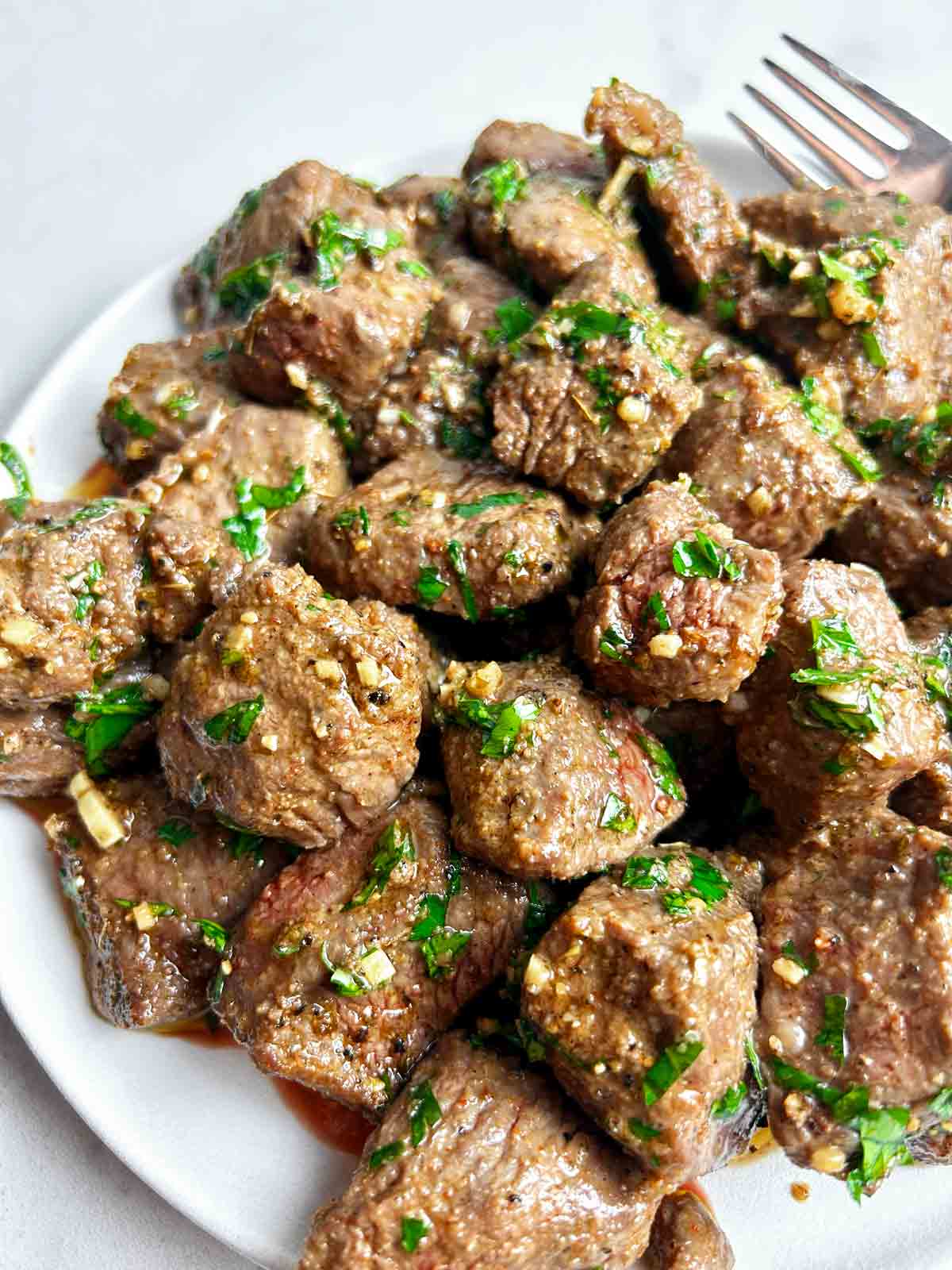 close up of air fryer steak bites with garlic butter on plate.
