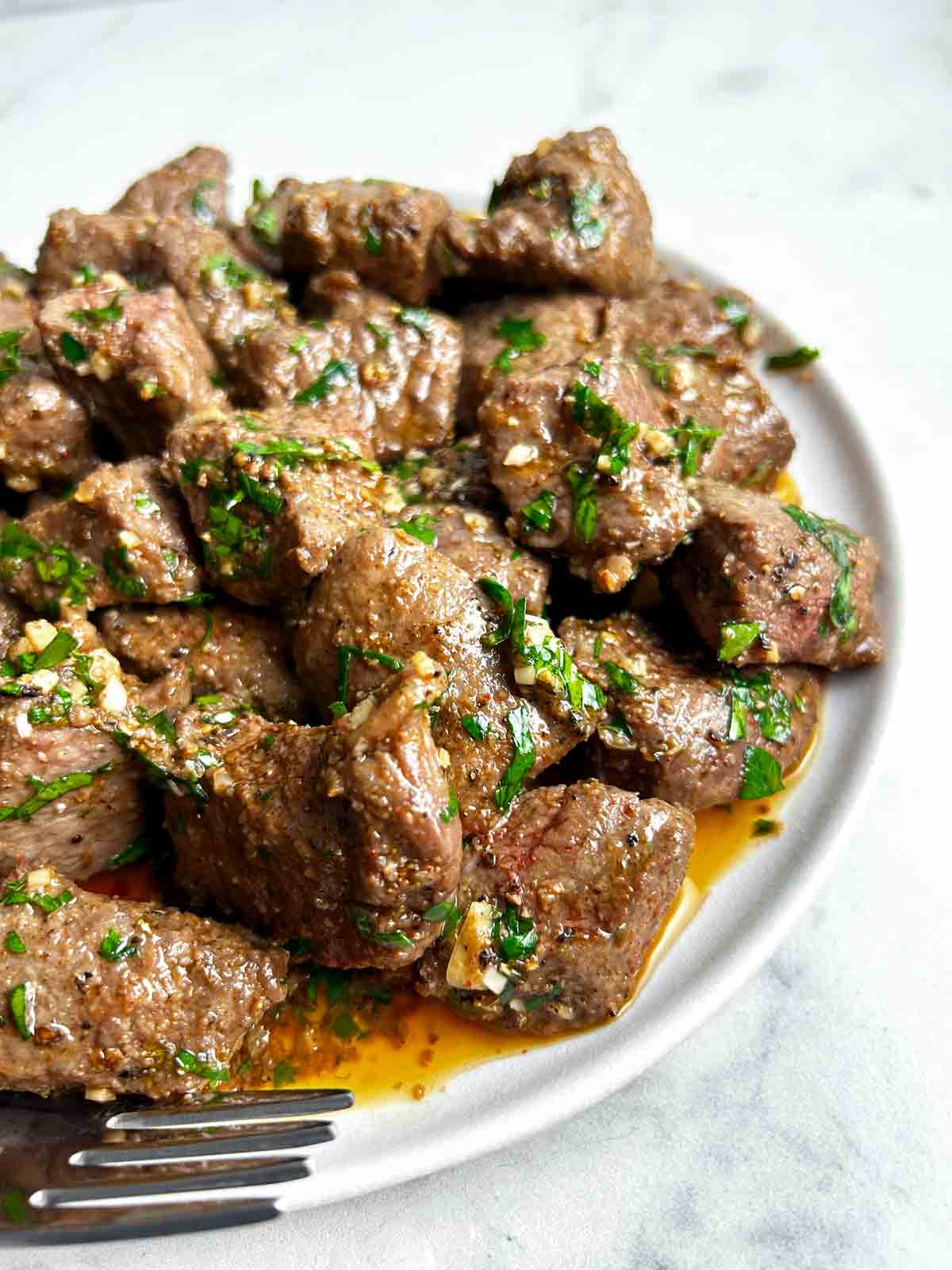 close up of air fryer steak bites with garlic butter on plate.