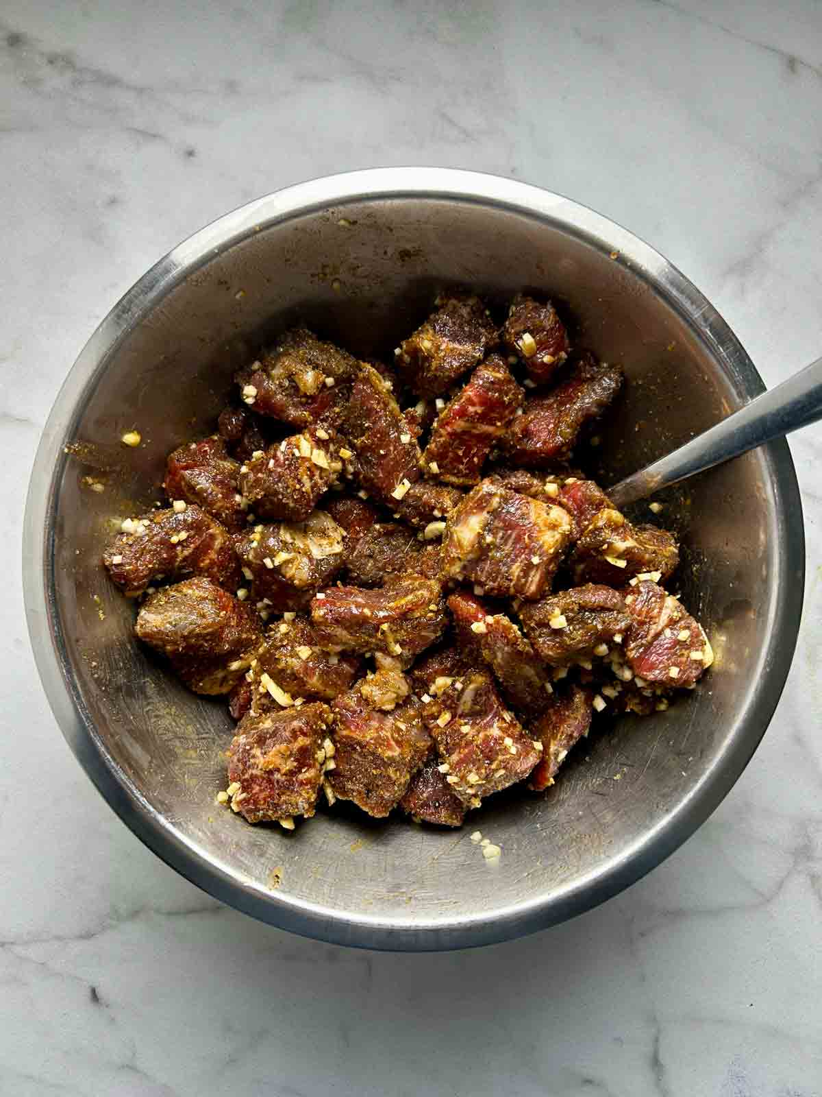 steak cubes tossed with spices and garlic in bowl.