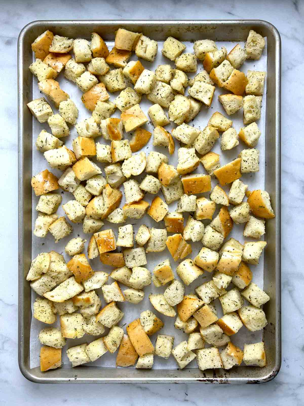 seasoned bread cubes spread onto baking sheet.