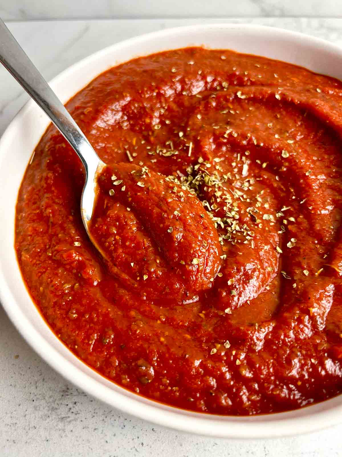 spoon lifting pizza sauce from bowl.