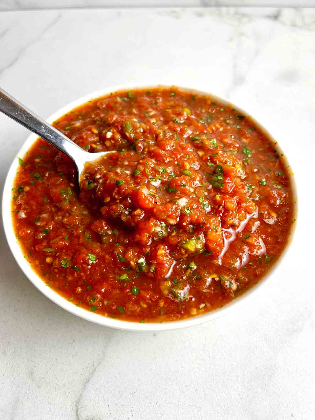 close up of spoon lifting salsa from bowl.