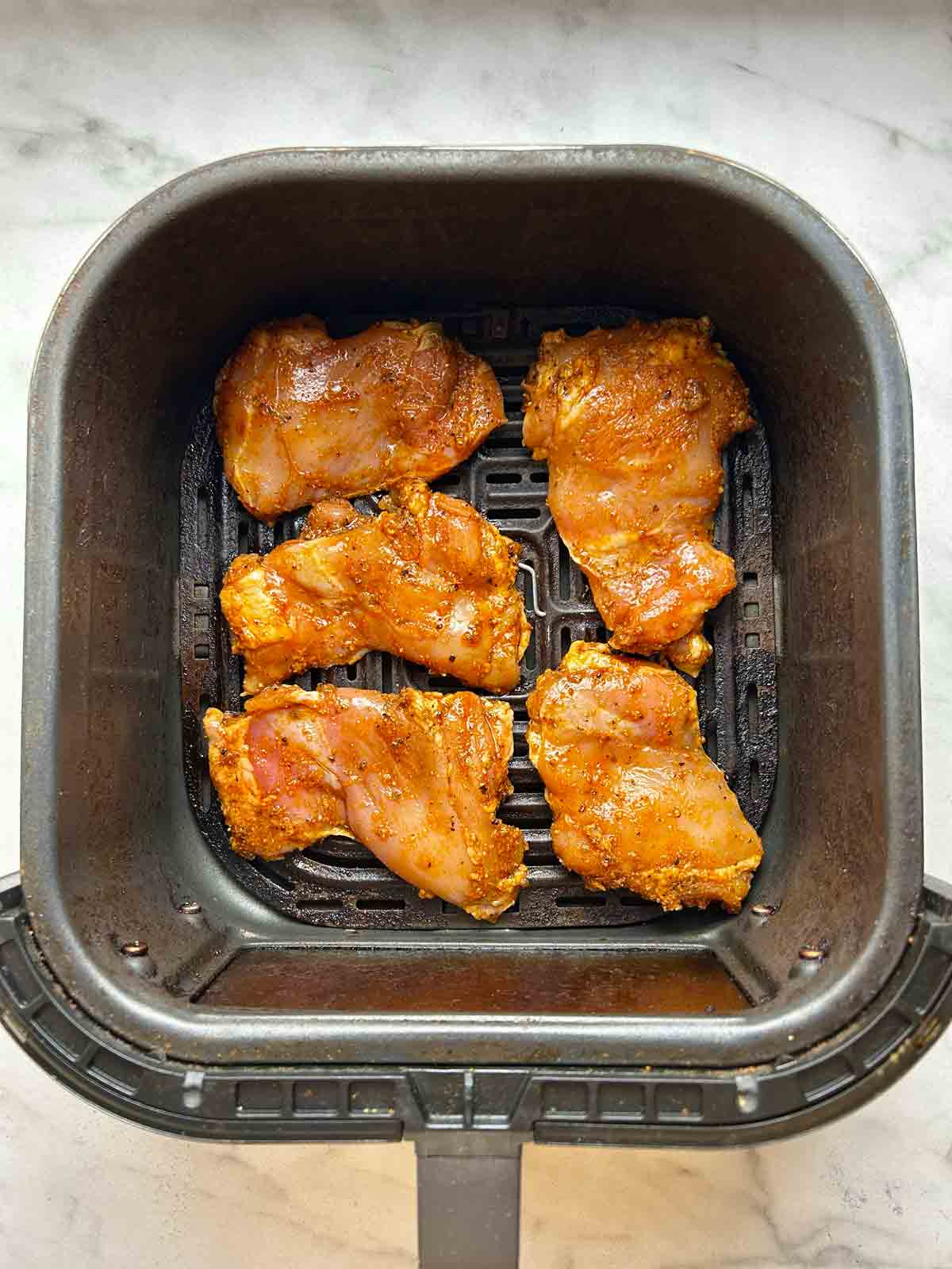 raw, seasoned chicken thighs in air fryer basket.