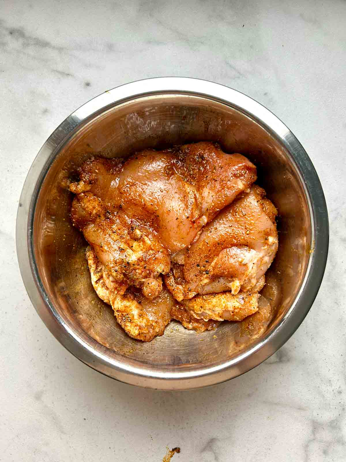 boneless chicken thighs mixed with spices in bowl.