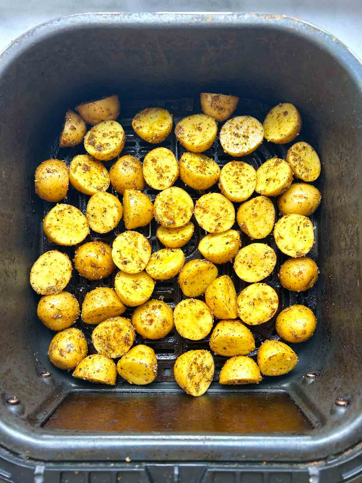 seasoned potatoes spread in air fryer basket.