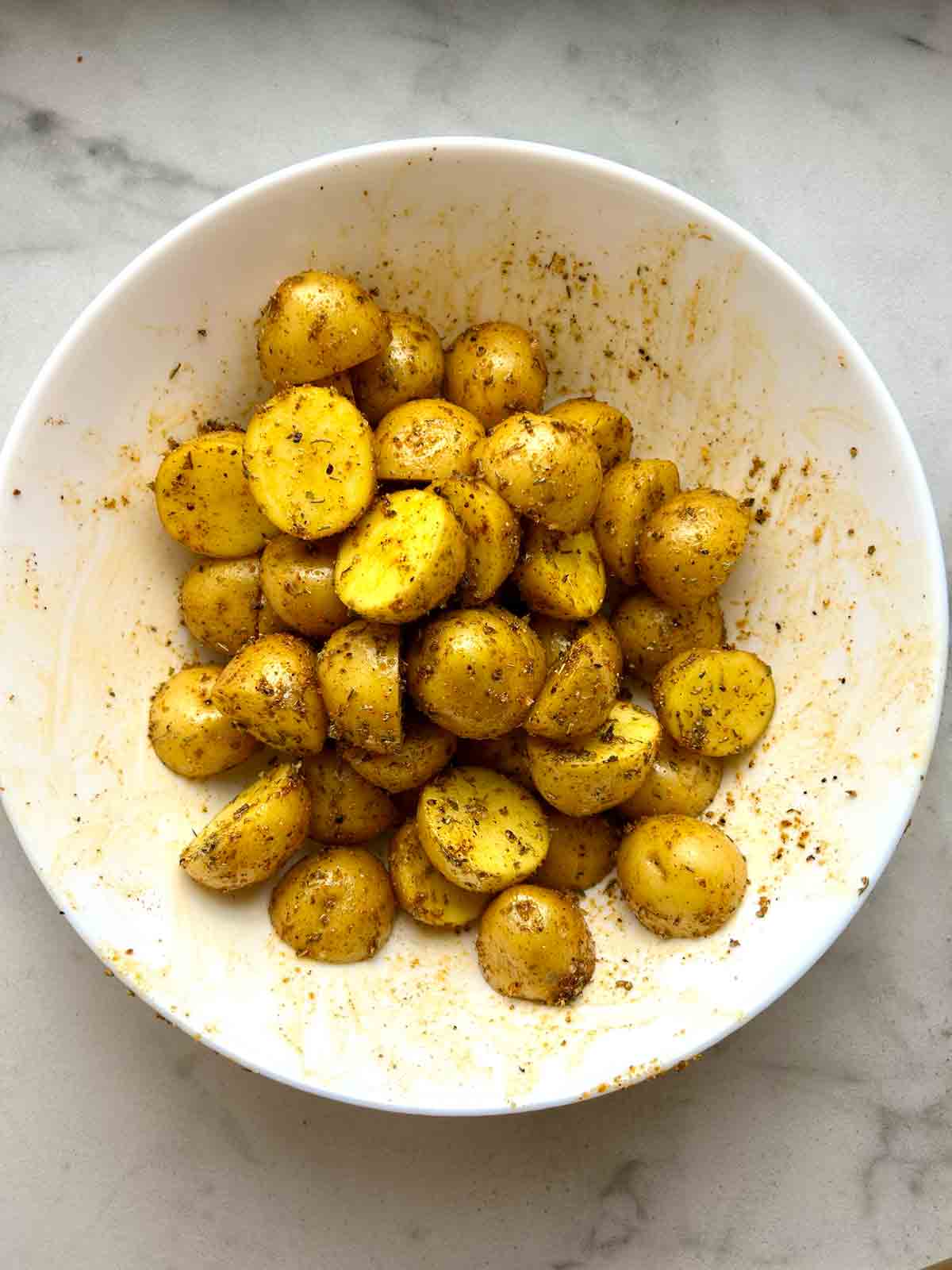 halved potatoes tossed with oil and seasonings in white bowl.