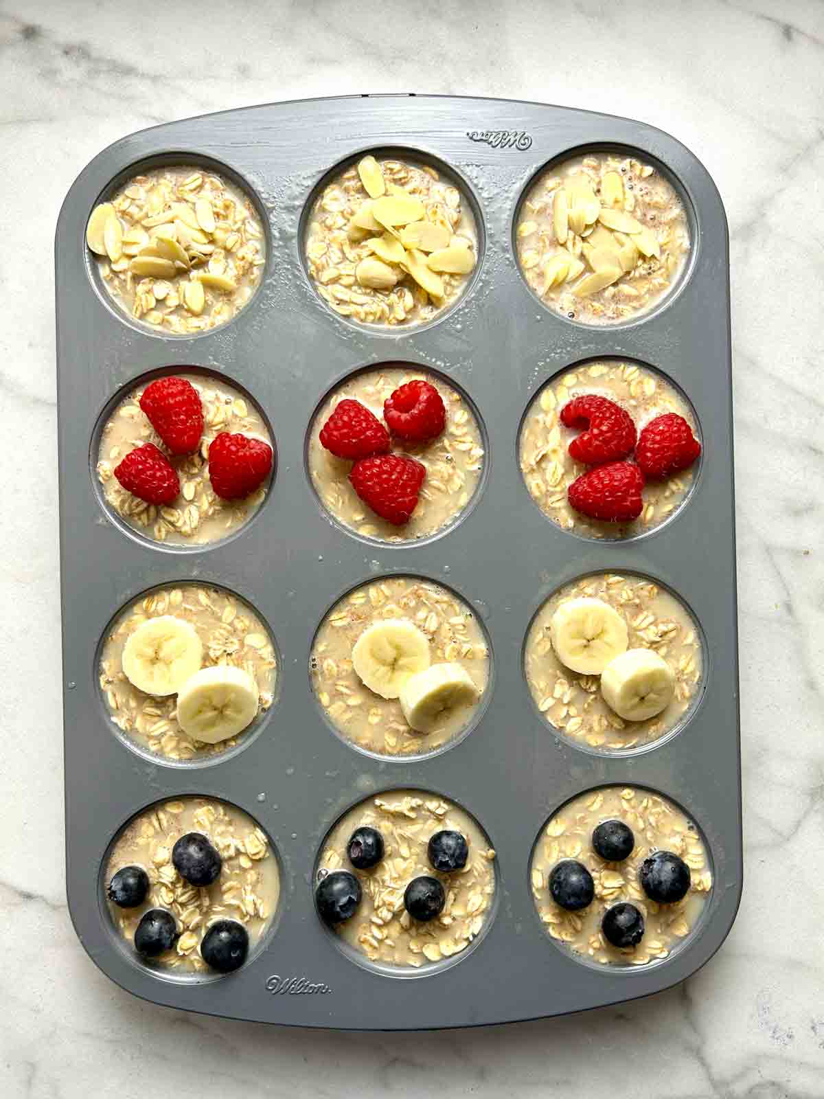 toppings added on top of oatmeal cups; sliced almonds, raspberries, bananas, and blueberries.