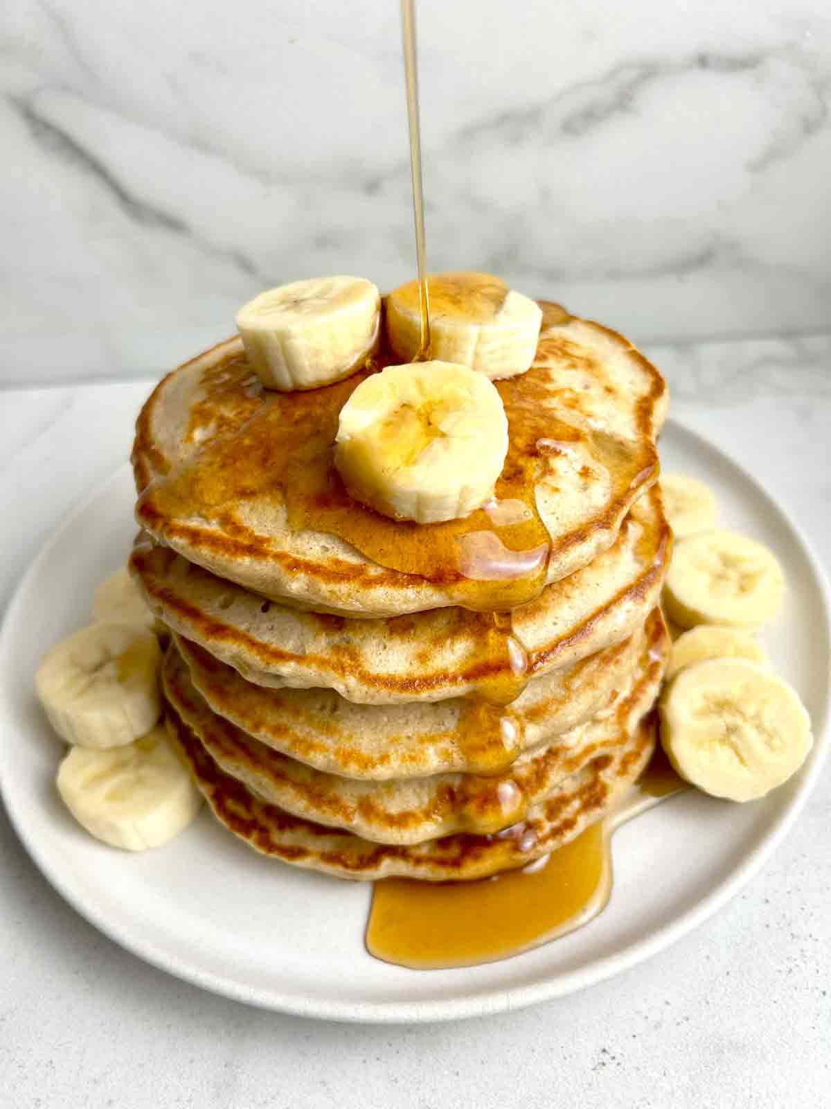 maple syrup being poured on stack of banana pancakes.