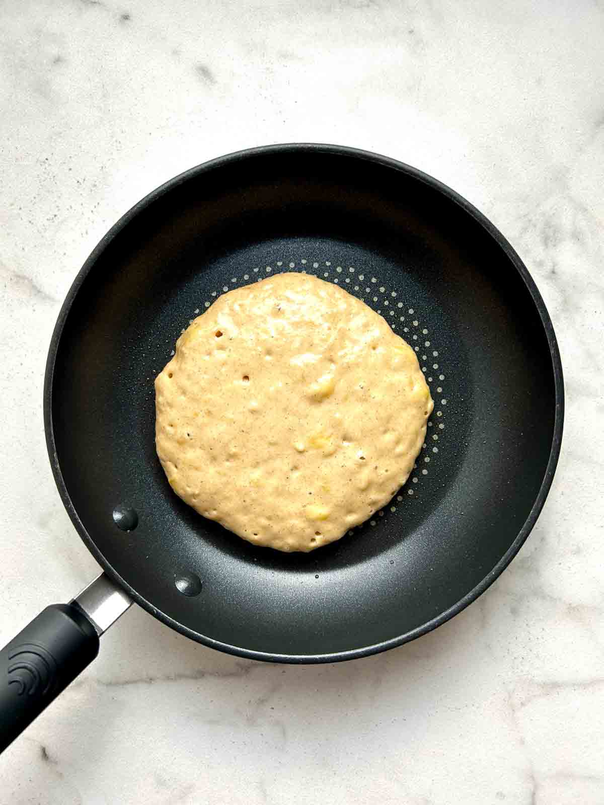 batter poured into pan; bubbles appearing on surface of pancake.